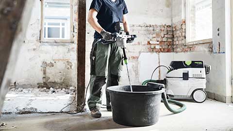 Una artigiana si trova in un cantiere e utilizza un miscelatore Festool in combinazione con un aspiratore.