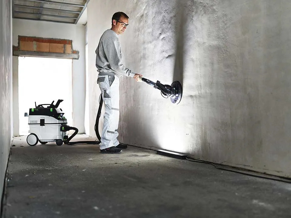 Un artigiano illumina una parete con l'aiuto della Luce di controllo dell'imbianchino e la leviga.